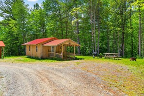 A wooden cabin with a red roof, a porch, and a picnic table in a forested area. - Soothing 1-bedroom COTTAGE with AC in charming Topsham (Topsham)