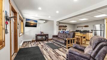 A cozy living room with a sofa, armchairs, a coffee table, and a TV mounted on the wall.