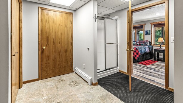 Habitación de hotel con puerta de madera, ducha, cama con manta a cuadros roja y negra y vistas al exterior.