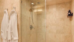 Ducha con mampara de vidrio, cabezal de ducha de mano y grifo empotrado en la pared.