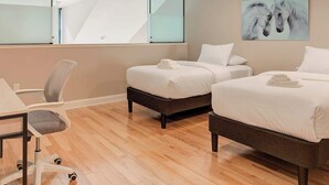 Habitación de hotel con dos camas, un escritorio, una silla y un ventanal grande.