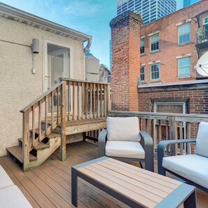 A wooden deck with outdoor furniture, including chairs and a table, and a staircase leading to a building entrance. - Luxury 3BR Near Rittenhouse + Roof Deck (Philadelphia)