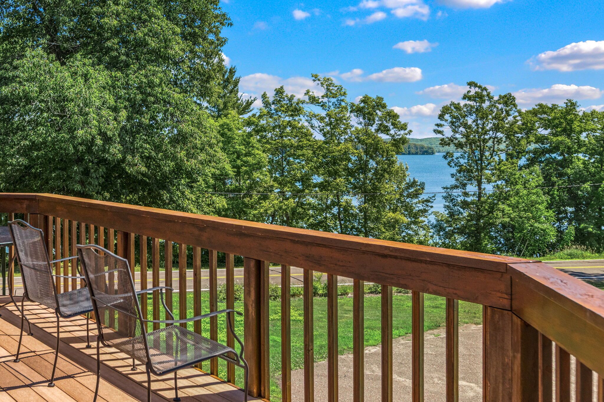 A wooden deck with metal chairs overlooking a lake.