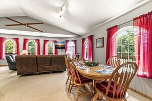 Een ruime eetruimte met een houten tafel en stoelen, een bank en grote ramen met rode gordijnen.
