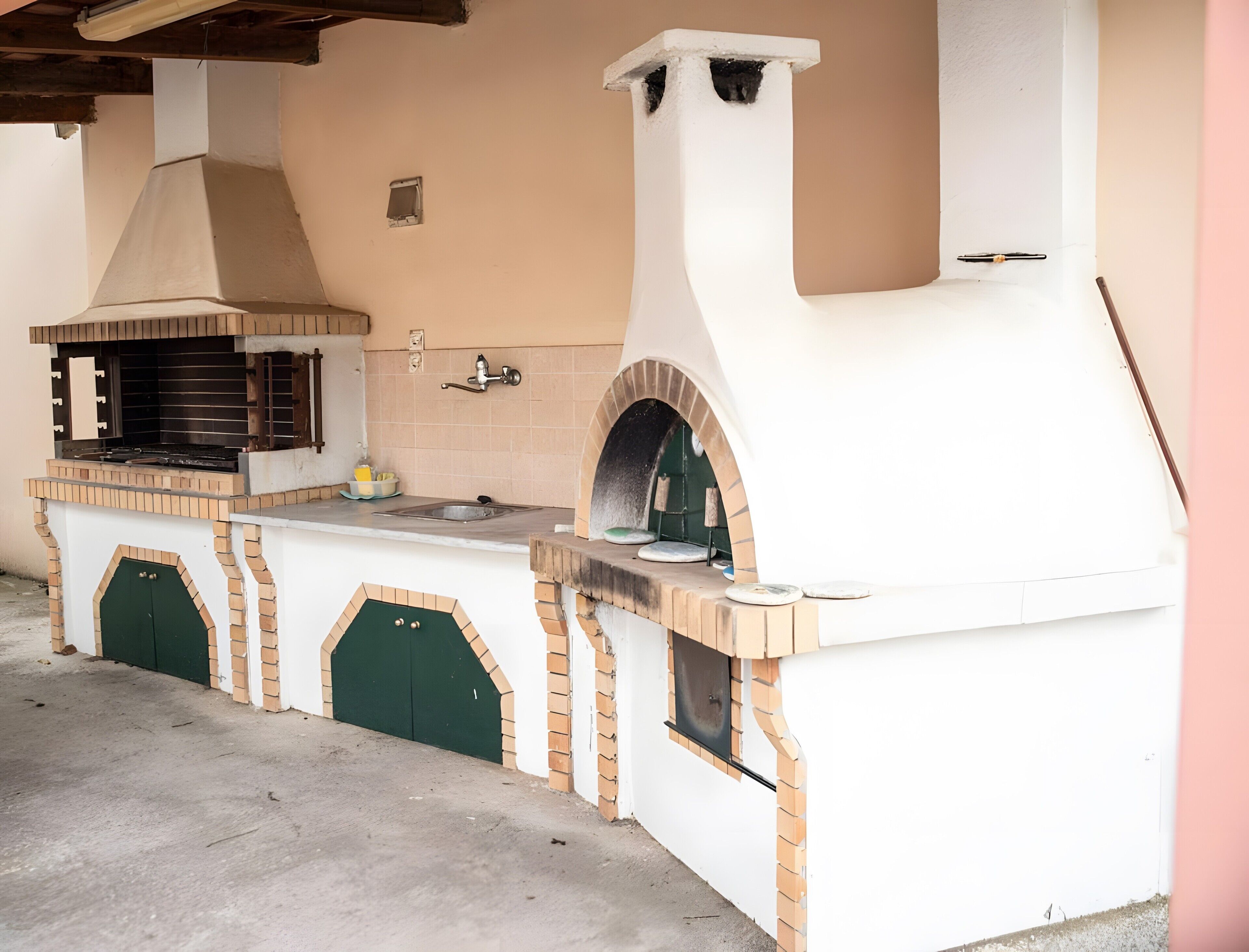 An outdoor kitchen with a grill, sink, and oven.