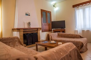 A living room with a fireplace, a television, and two covered sofas. - Country House 'Evoia Village House' with Mountain View, Wi-Fi and Air Conditioning (Neochori)