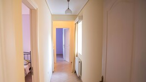 Ein schmaler Flur mit einem Bett und einem Heizkörper links, einer Tür rechts und einer Deckenleuchte.