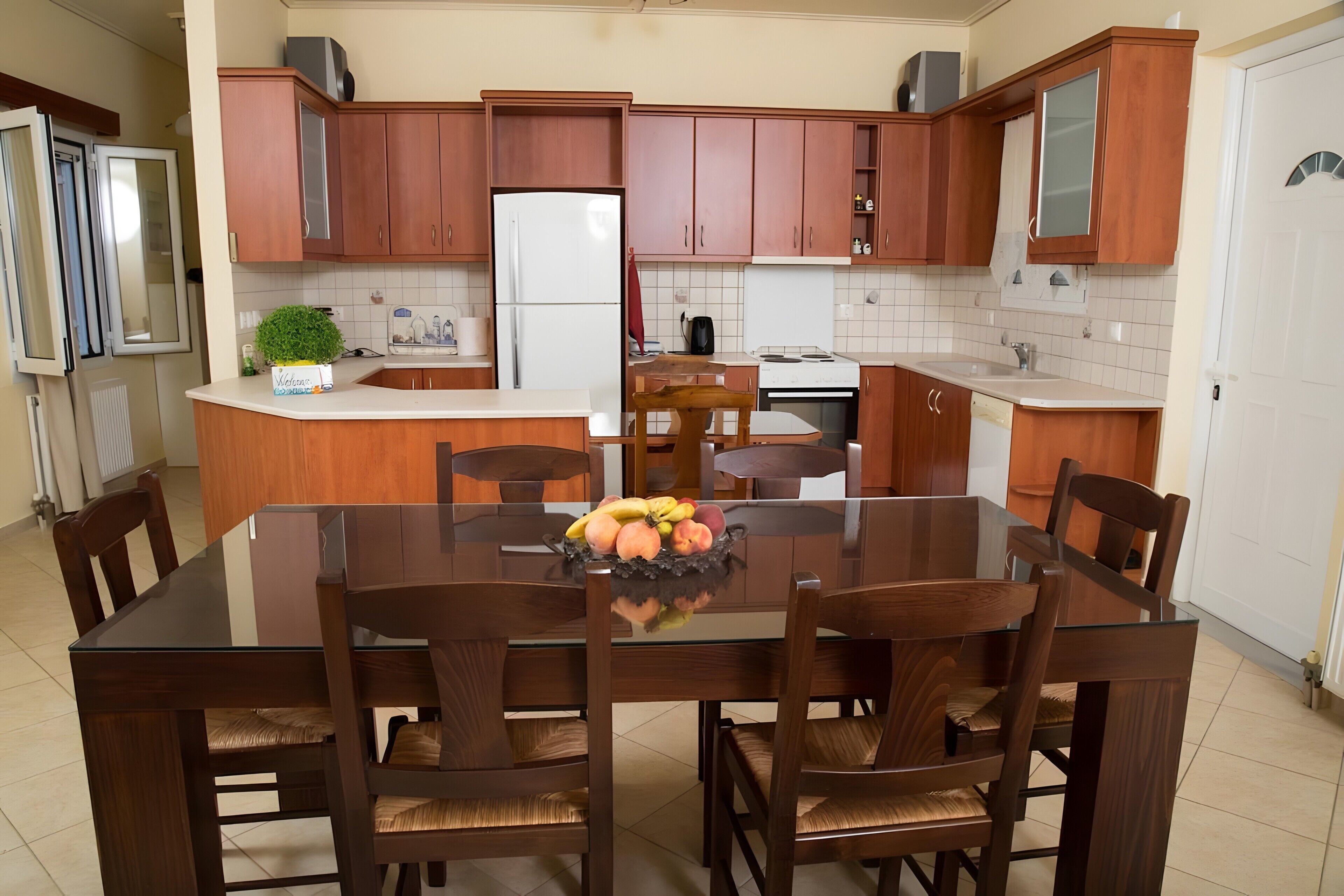 A modern kitchen with wooden cabinets, a central island with a fruit bowl, and a dining area with chairs.