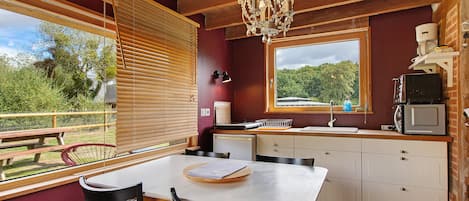 A kitchen with a dining table, chairs, a chandelier, a window with a view, and a microwave.