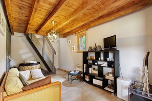 Un salon chaleureux avec un plafond en bois, un escalier, un téléviseur et une bibliothèque.