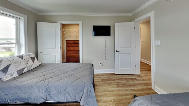 Un dormitorio con una cama, un televisor montado en la pared y un armario con puerta de madera.