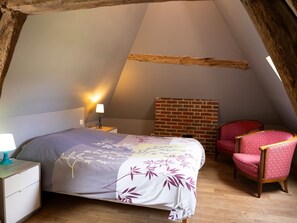 Ein Schlafzimmer im Dachgeschoss mit schrägen Wänden, einem Bett mit blumigem Bettzeug, einem roten Sessel und einer Backsteinwand.