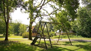 A swing set in a grassy park area with trees and a building in the background. - The Old Stable – In the Heart of 20 Hectares of Greenery (Flancourt-Crescy-en-Roumois)