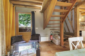 Une pièce comprenant une table à plateau de verre, une chaise, un canapé, une cheminée, un escalier et une fenêtre avec des rideaux.