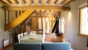 A cozy room with a wooden ceiling, a brick wall, and a dining area with a table and chairs. - The Old Stable – In the Heart of 20 Hectares of Greenery (Flancourt-Crescy-en-Roumois)