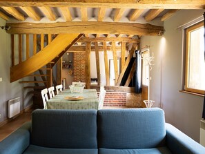 Ein gemütliches Zimmer mit Holzbalkendecke, einer Ziegelwand und einem Essbereich mit Tisch und Stühlen.