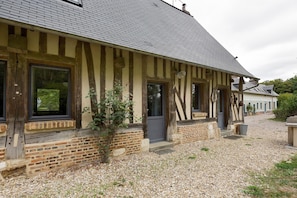 A traditional timber-framed building with a gravel driveway and a small garden area. - The Old Stable – In the Heart of 20 Hectares of Greenery (Flancourt-Crescy-en-Roumois)