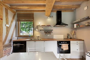 A modern kitchen with wooden beams, a Bosch stove, and a window overlooking greenery. - The Old Stable – In the Heart of 20 Hectares of Greenery (Flancourt-Crescy-en-Roumois)