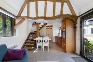 Un intérieur moderne avec des poutres apparentes, un escalier, un coin repas et une cuisine.