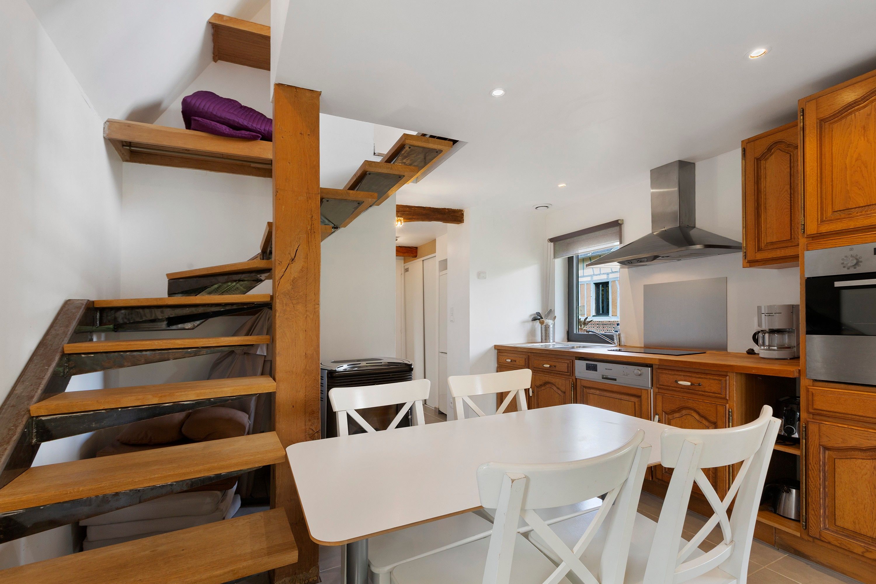 Una cocina moderna con armarios de madera, una mesa de comedor con sillas y una escalera con un cojín morado.