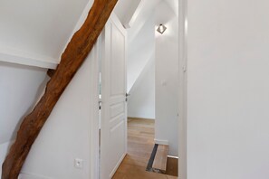 A staircase with a wooden beam, white walls, and a door leading to a room with a light switch and a power outlet.