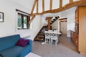 A modern interior with a blue sofa, wooden staircase, and a kitchen area.