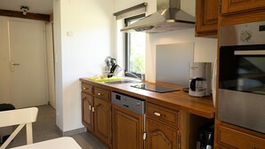 A modern kitchen with wooden cabinets, a stainless steel range hood, a dishwasher, and a coffee maker. - The Cottage – In the Heart of a 20-Hectare Estate (Flancourt-Crescy-en-Roumois)