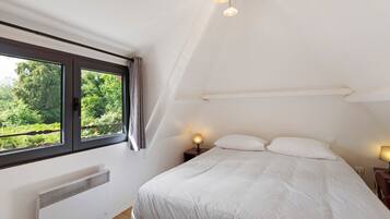 Un dormitorio con un ventanal grande, una cama con ropa de cama blanca, una mesita de noche con lámpara y una lámpara en el techo.
