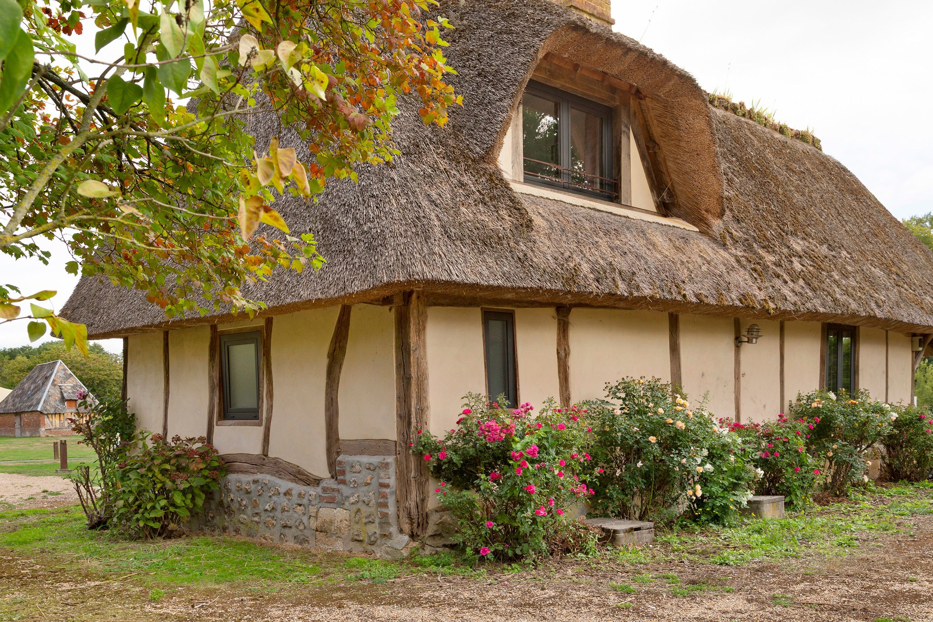 Ein traditionelles Haus mit einem Reetdach, Stein Fundament, Holzbalken und einem kleinen Fenster.