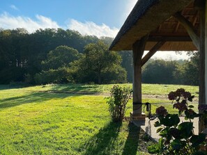 Ein Pavillon mit einem Reetdach, der auf ein grünes Feld mit Bäumen im Hintergrund blickt.