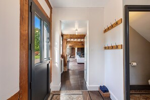 A hallway with a wooden door, a coat rack, and a view into a room with a fireplace. - La Longère – In the Heart of a 20-Hectare Estate (Flancourt-Crescy-en-Roumois)