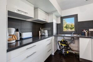 A modern kitchen with white cabinets, a coffee maker, a toaster, and a window with a view of trees. - La Longère – In the Heart of a 20-Hectare Estate (Flancourt-Crescy-en-Roumois)