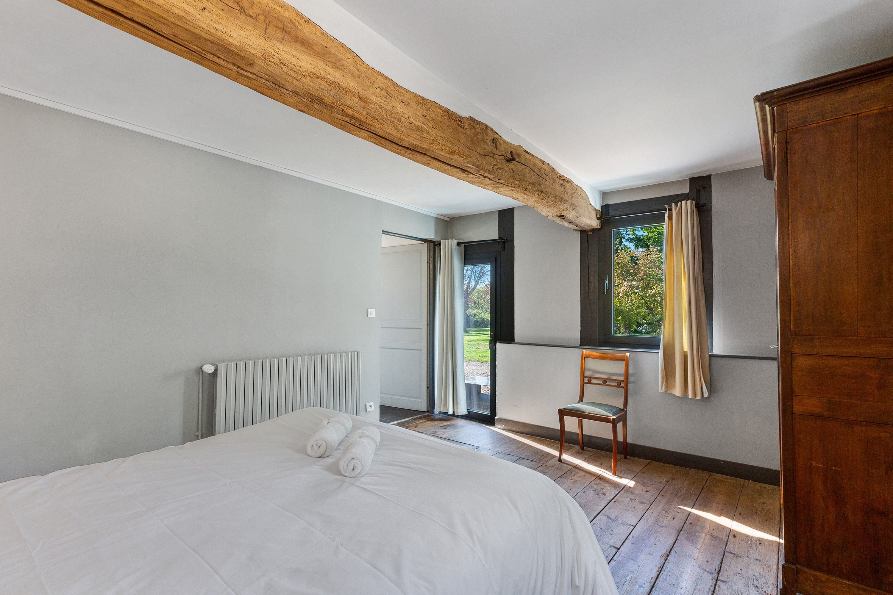 Une chambre à coucher avec un grand lit, une chaise en bois, une fenêtre avec des rideaux et un radiateur.