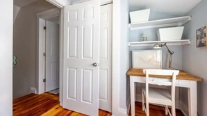 Una habitación con suelo de madera, puerta y estanterías blancas, y un escritorio con silla.
