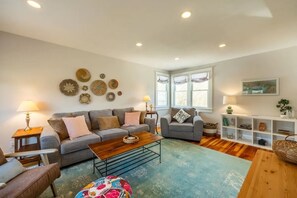 A living room with two sofas, a coffee table, a patterned rug, and a bookshelf with decorative items. - Dharma Cottage - A Quiet 3BR Coastal Getaway in Historic Fairhaven (Fairhaven)