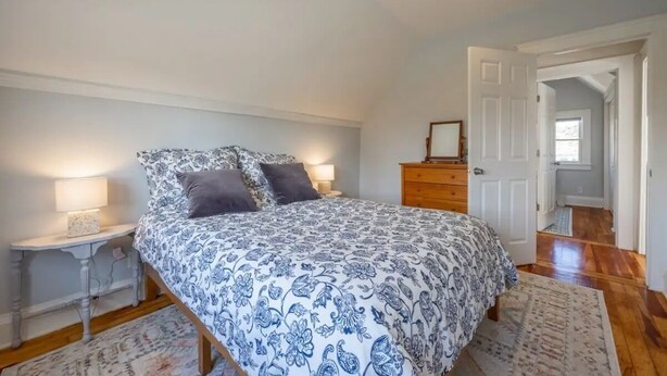 Un dormitorio con cama, mesitas de noche, cómoda y una puerta que da a otra habitación.