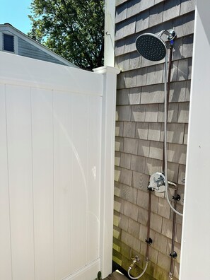 A white wooden fence, a metal showerhead, and a hose attached to a wall with wooden siding. - Dharma Cottage - A Quiet 3BR Coastal Getaway in Historic Fairhaven (Fairhaven)
