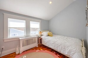 Ein Schlafzimmer mit einem Bett, einem Fenster, einer Heizung und einem Nachttisch.