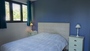 Ein Schlafzimmer mit einem Bett, zwei Nachttischen, einem Fenster mit Vorhängen und einem Kopfteil.