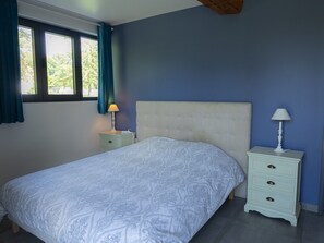 Ein Schlafzimmer mit einem Bett, zwei Nachttischen, einem Fenster mit Vorhängen und einem Kopfteil.