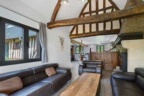 A spacious living area with a high ceiling, exposed wooden beams, leather sofas, and a view through a large window. - La Roselière – In the Heart of 20 Hectares of Greenery (Flancourt-Crescy-en-Roumois)