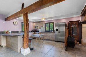 A modern kitchen with a central island, wooden beams, and a view of the outdoors through large windows. - La Roselière – In the Heart of 20 Hectares of Greenery (Flancourt-Crescy-en-Roumois)