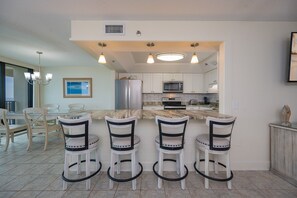 A modern kitchen with a central island, bar stools, and a dining area with chairs. - Phoenix Vii 7207 1 Bedroom Condo (Orange Beach)
