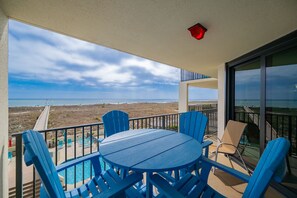 A balcony with a view of the beach, a pool, and a table with chairs. - Phoenix Vii 7207 1 Bedroom Condo (Orange Beach)