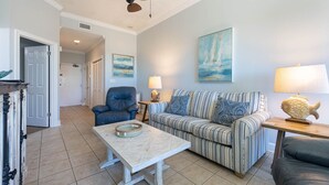 A living room with a striped sofa, a blue armchair, a coffee table, and a lamp. - Phoenix Vii 7102 1 Bedroom Condo (Orange Beach)