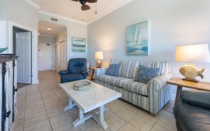 A living room with a striped sofa, a blue armchair, a coffee table, and a lamp. - Phoenix Vii 7102 1 Bedroom Condo (Orange Beach)