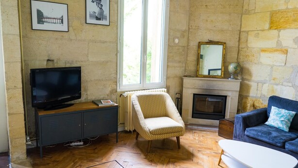 Uma sala de estar com televisão, lareira, sofá, poltrona e janela.
