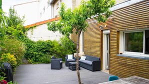 Um pátio externo com deck de madeira, uma pequena árvore e mobiliário de exterior, incluindo um sofá e cadeiras.