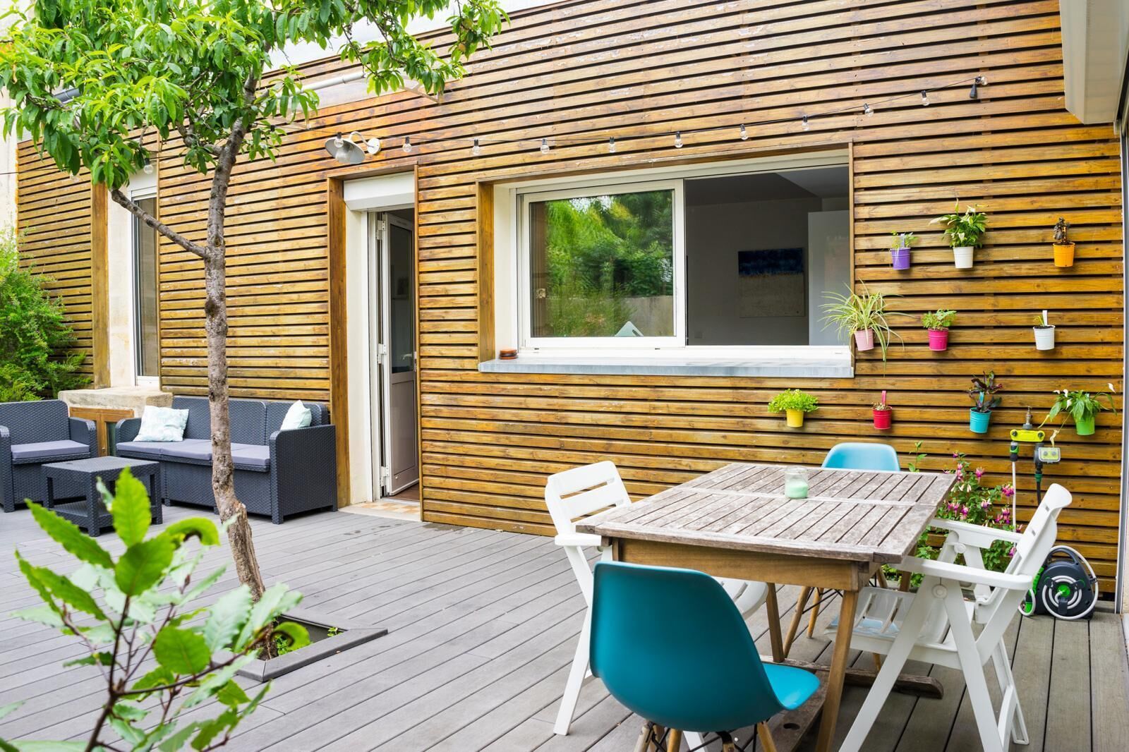 Eine Terrasse im Freien mit Holzboden, einem Tisch, Stühlen und einer Sitzecke mit Sofas.