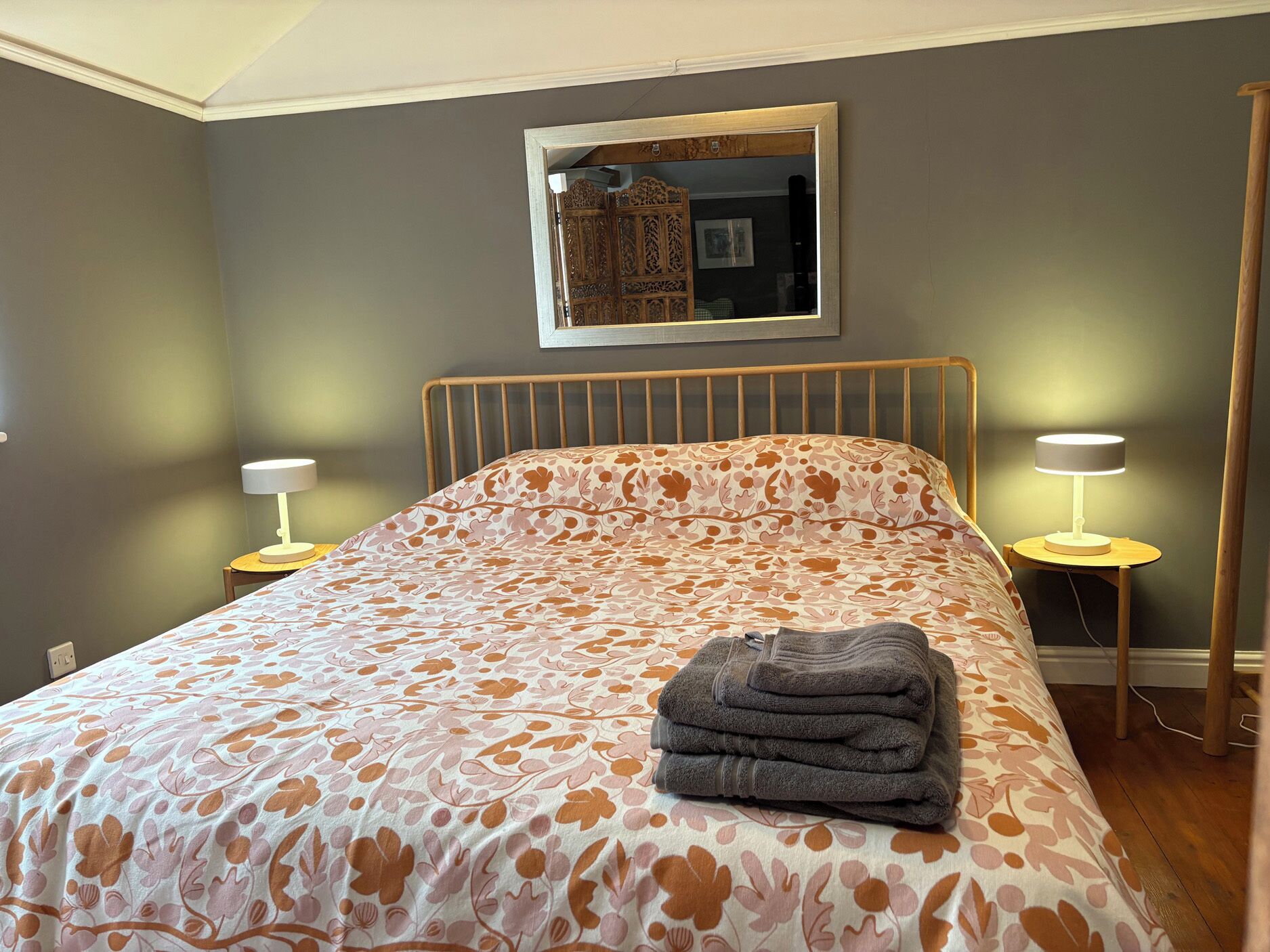 A bedroom with a bed, two bedside lamps, a mirror, and a folded towel.